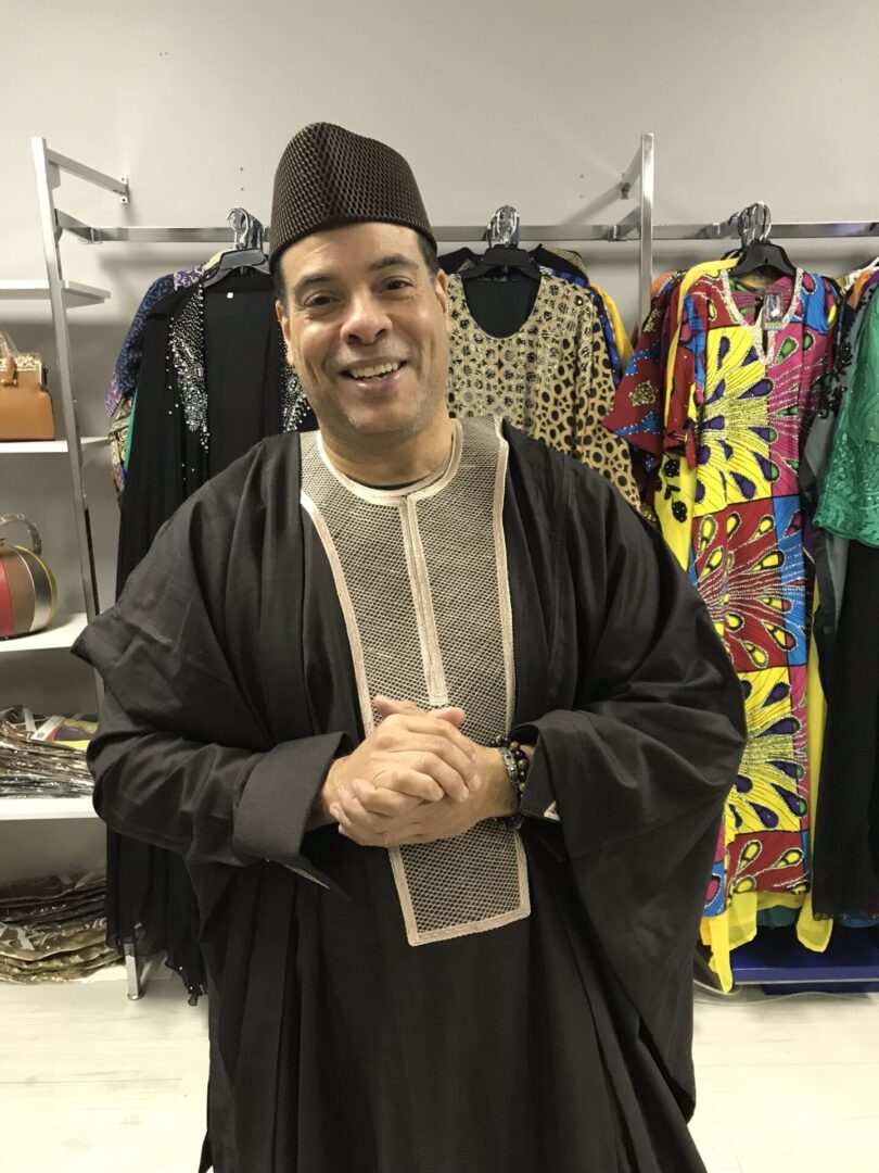 A man in an african outfit standing next to clothes.