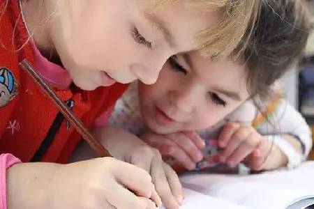 Two children are writing on a piece of paper.